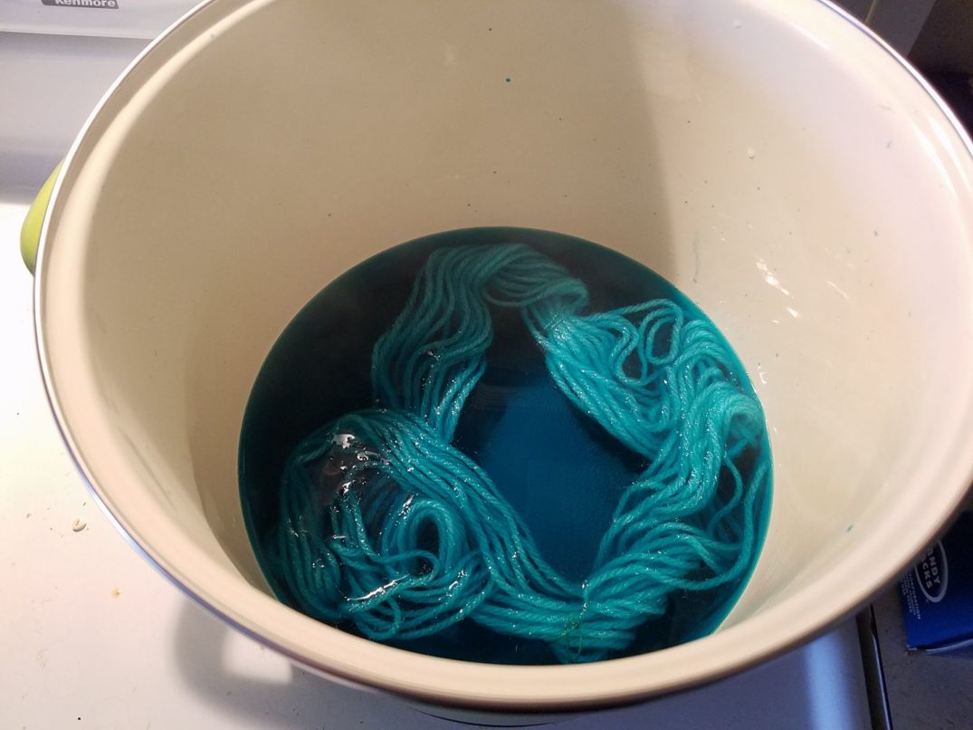 A skein of yarn in a dye pot, being dyed blue. There's still lots of dye left in the water.